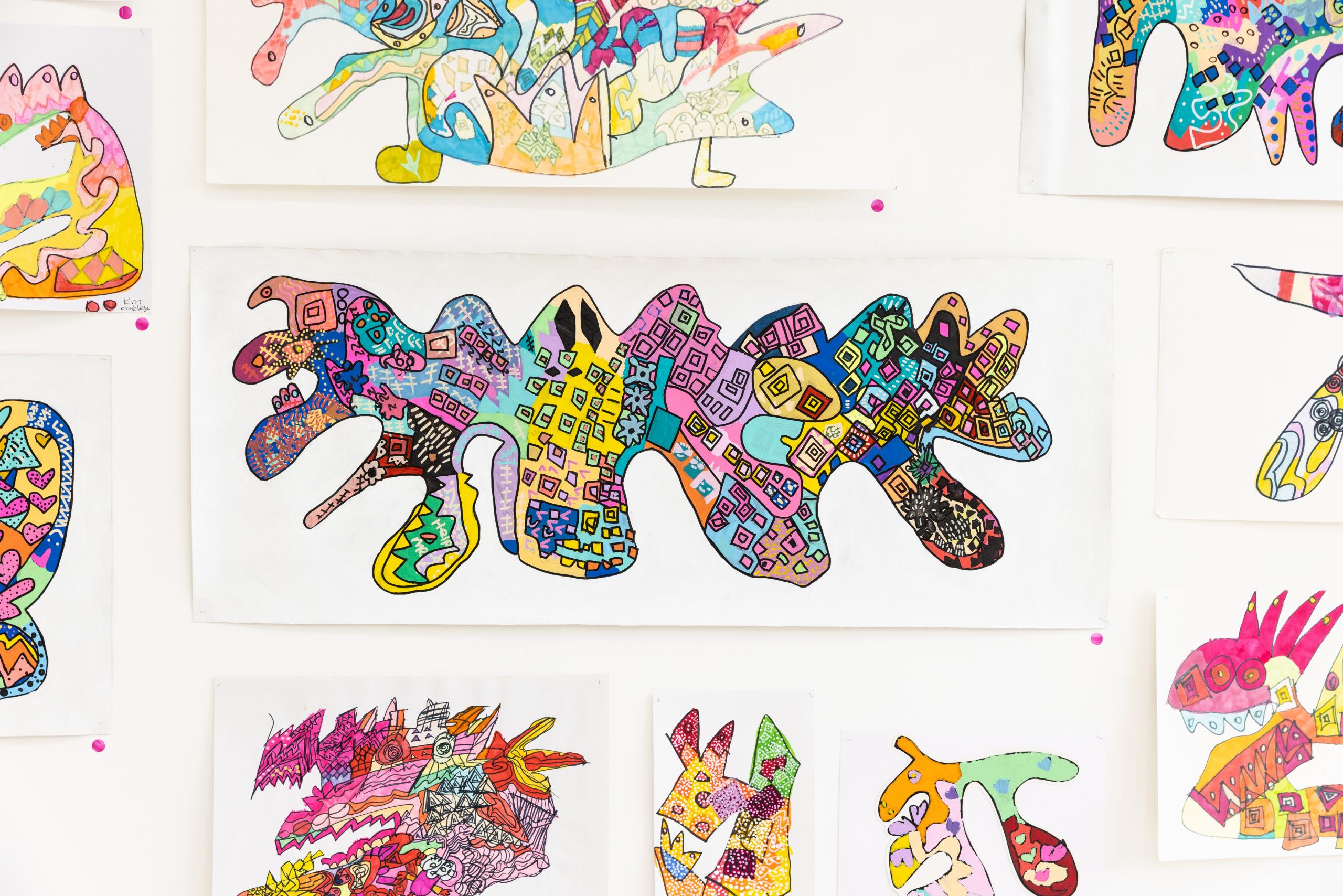 The images shows a collection of colorful drawings inspired by dragon shapes. The central piece is a large, irregularly shaped figure filled with various geometric patterns and vibrant colors, including pink, blue, yellow, green and black. Surrounding this central piece are several other similar abstract dragon- like shapes, each filled with different patterns and colors. The overall style is whimsical and playful, with a focus in bright, contrasting colors and intricate designs.