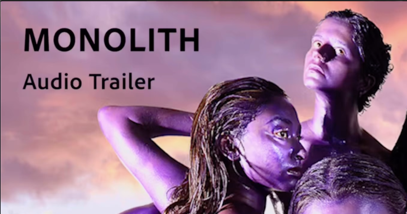 a still image of 4 women with purple-painted skin, intertwined and posing closely together. Their bodies and faces are covered in shiny, metallic purple paint, and they are looking in different directions with serious expressions. The background is a dramatic sky with clouds lit by a sunset or sunrise, casting an orange and pink glow. In the top left corner, black text reads: MONOLITH Audio Trailer